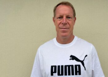Mann in weißem Puma T-Shirt vor neutralem Hintergrund, Porträtfoto