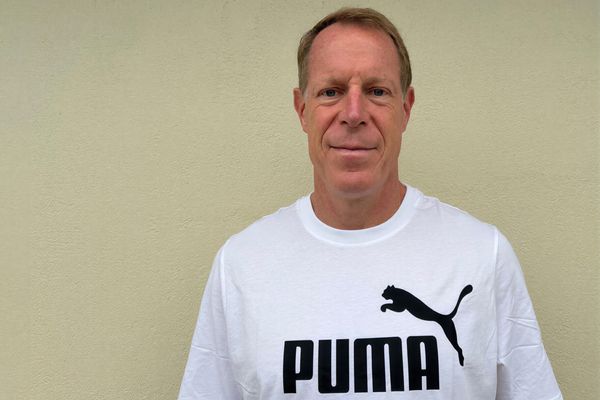 Mann in weißem Puma T-Shirt vor neutralem Hintergrund, Porträtfoto