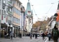 Fußgängerzone in Freiburgs Innenstadt mit historischem Turm, Geschäften und Passanten