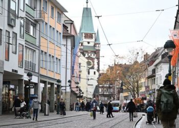 Fußgängerzone in Freiburgs Innenstadt mit historischem Turm, Geschäften und Passanten