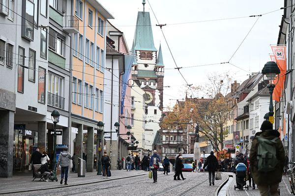 Fußgängerzone in Freiburgs Innenstadt mit historischem Turm, Geschäften und Passanten