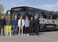Gruppenfoto von etwa zehn Personen vor einem schwarzen Bus mit Schuhstadt-Schriftzug bei Tageslicht.