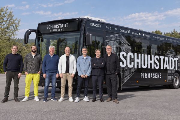 Gruppenfoto von etwa zehn Personen vor einem schwarzen Bus mit Schuhstadt-Schriftzug bei Tageslicht.