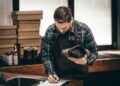 Handwerker in Werkstatt poliert schwarzen Schuh, Werkzeuge und Materialien im Hintergrund