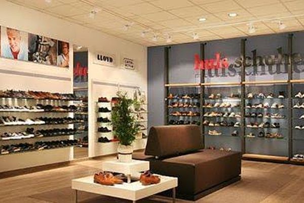 Moderne Schuhgeschäft-Innenansicht mit beleuchteten Schuhregalen an den Wänden, zentralem Holztisch und großflächigen dunklen Vitrinen