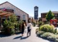 Belebter Platz im Fashion-Outlet Landquart mit modernen Gebäuden, grünen Pflanzen und Besuchern beim Spaziergang