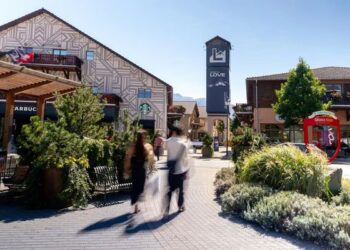 Belebter Platz im Fashion-Outlet Landquart mit modernen Gebäuden, grünen Pflanzen und Besuchern beim Spaziergang