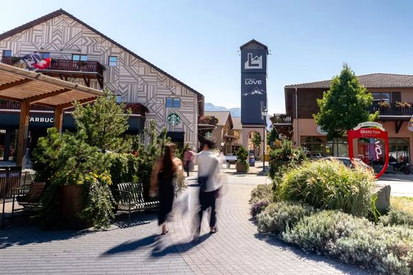 Belebter Platz im Fashion-Outlet Landquart mit modernen Gebäuden, grünen Pflanzen und Besuchern beim Spaziergang