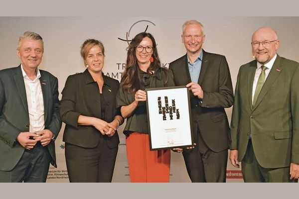 Fünf Personen in Business-Kleidung halten ein Zertifikat und eine Urkunde in die Kamera, anlässlich einer Preisverleihung für Ehrenamt.