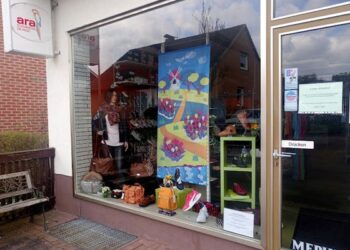 Schaufenster eines Schuhfachgeschäfts mit bunten Auslagen, Schuhen und Dekorationen hinter Glasfront an Backsteingebäude.