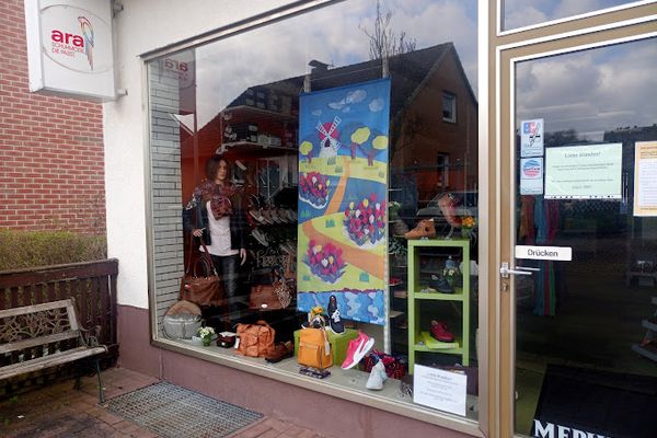 Schaufenster eines Schuhfachgeschäfts mit bunten Auslagen, Schuhen und Dekorationen hinter Glasfront an Backsteingebäude.