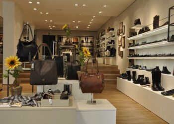 Modernes Schuhgeschäft mit Ausstellungsfläche, Regalen an den Wänden mit Schuhen und Accessoires, Verkaufstischen mit Handtaschen und Schuhen, Dekoration