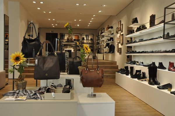 Modernes Schuhgeschäft mit Ausstellungsfläche, Regalen an den Wänden mit Schuhen und Accessoires, Verkaufstischen mit Handtaschen und Schuhen, Dekoration